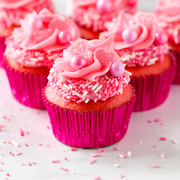 A photo of the Let's Go Party Sprinkle Mix, featuring a variety of hot pink, light pink, and white sprinkles, as well as specialty pieces like pink wafer paper diamonds, shoes, handbags, and hearts.