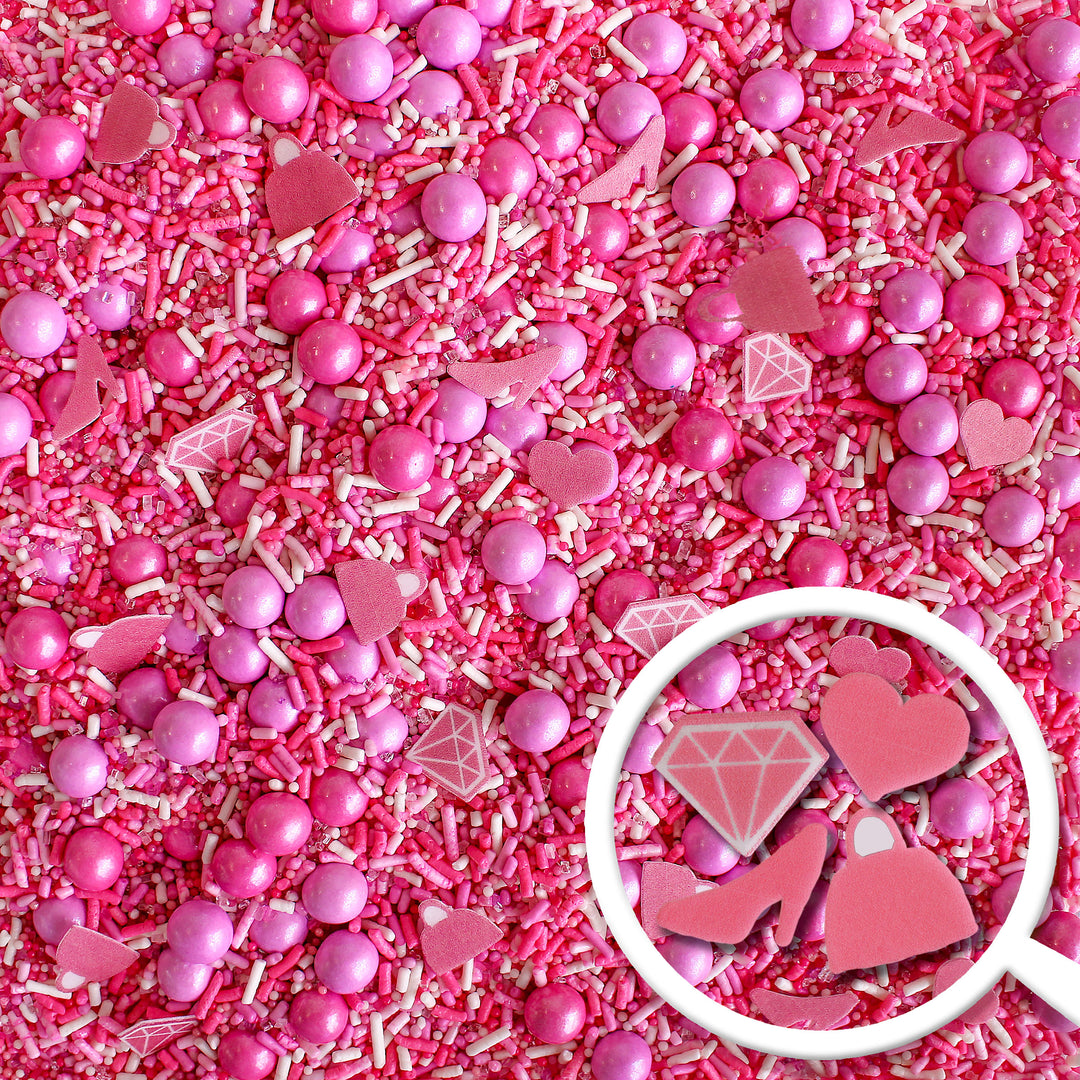 A photo of the Let's Go Party Sprinkle Mix, featuring a variety of hot pink, light pink, and white sprinkles, as well as specialty pieces like pink wafer paper diamonds, shoes, handbags, and hearts.