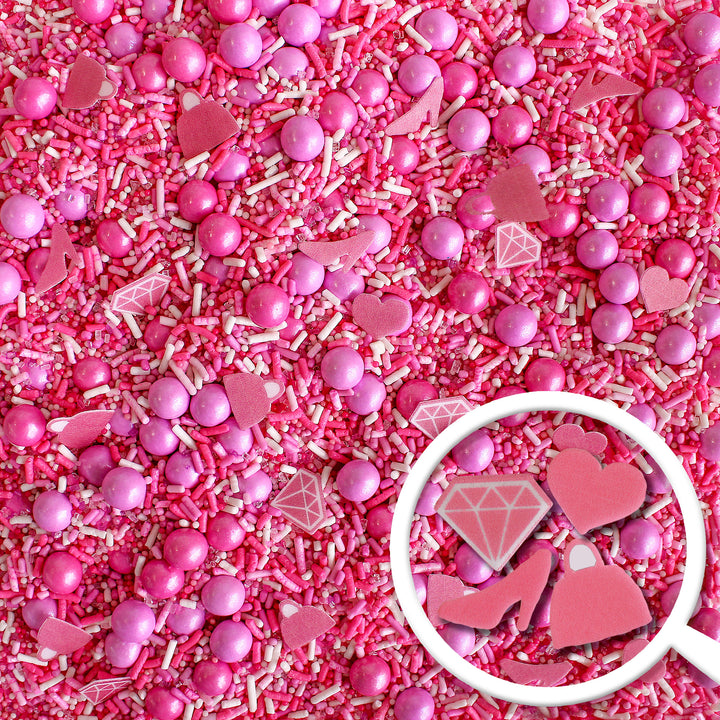 A photo of the Let's Go Party Sprinkle Mix, featuring a variety of hot pink, light pink, and white sprinkles, as well as specialty pieces like pink wafer paper diamonds, shoes, handbags, and hearts.