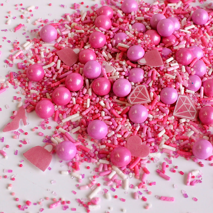 A photo of the Let's Go Party Sprinkle Mix, featuring a variety of hot pink, light pink, and white sprinkles, as well as specialty pieces like pink wafer paper diamonds, shoes, handbags, and hearts.
