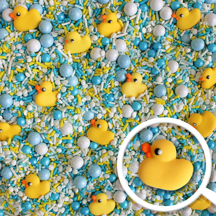 Close-up of Bubble Bath Sprinkle Mix featuring a variety of white, blue, and yellow sprinkles, as well as adorable royal icing rubber ducks.