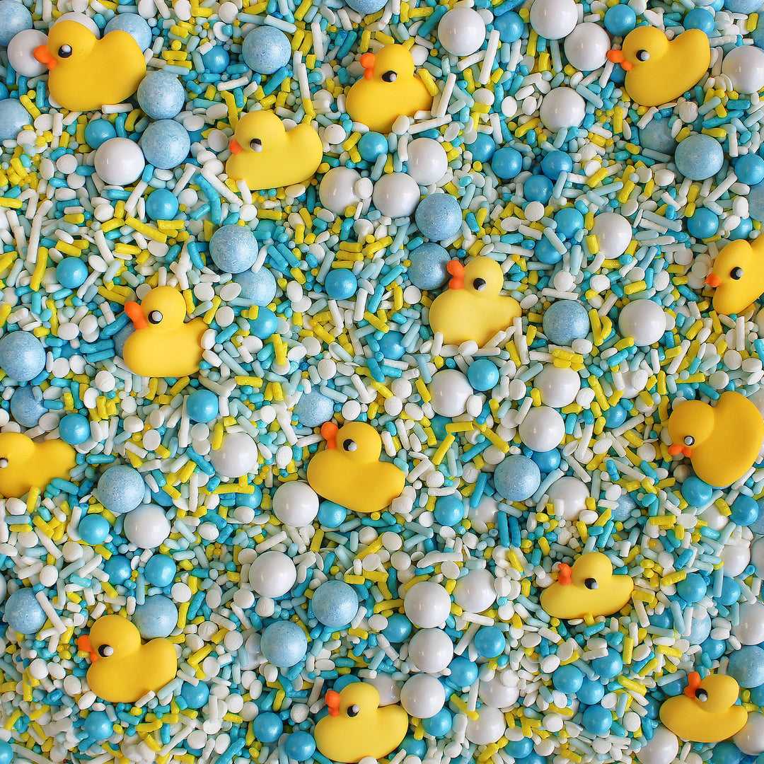 Close-up of Bubble Bath Sprinkle Mix featuring a variety of white, blue, and yellow sprinkles, as well as adorable royal icing rubber ducks.