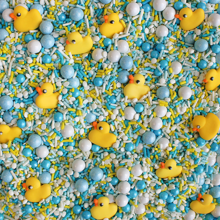 Close-up of Bubble Bath Sprinkle Mix featuring a variety of white, blue, and yellow sprinkles, as well as adorable royal icing rubber ducks.