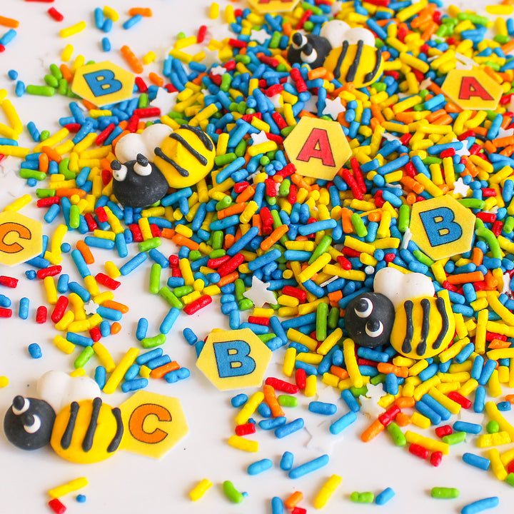 Spelling Bee Sprinkle Mix - A vibrant mix of red, green, yellow, and blue sprinkles with wafer ABC honeycomb letters and royal icing bees.