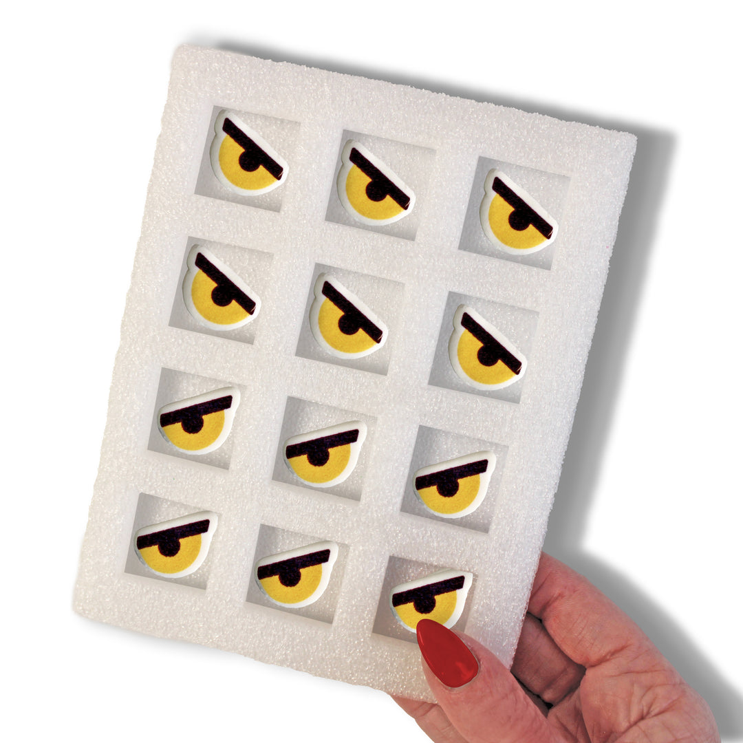 A set of 12 hand-piped royal icing decorations with iconic yellow mean eyes, ideal for topping cakes, cupcakes, and other treats.