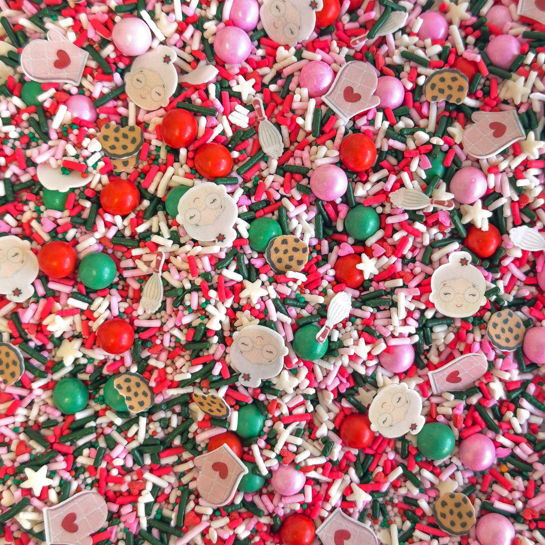 Colorful sprinkle mix featuring pink, red, and green shapes including cookies, mittens, and a granny, ideal for Christmas baking.