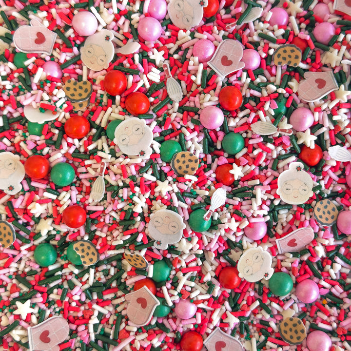 Colorful sprinkle mix featuring pink, red, and green shapes including cookies, mittens, and a granny, ideal for Christmas baking.