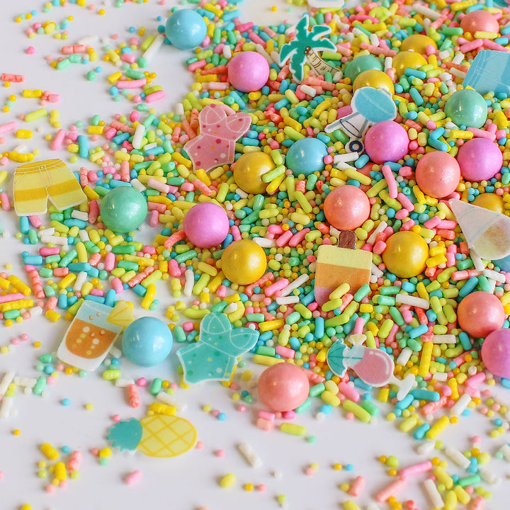 A close-up photo of Palm Springs Sprinkle Mix with a variety of colorful sprinkles, including specialty pieces like wafer swimsuits, palm trees, snow cones, umbrella drinks, and bbq grills. Perfect for decorating cakes, cookies, cupcakes, and even ice cream!