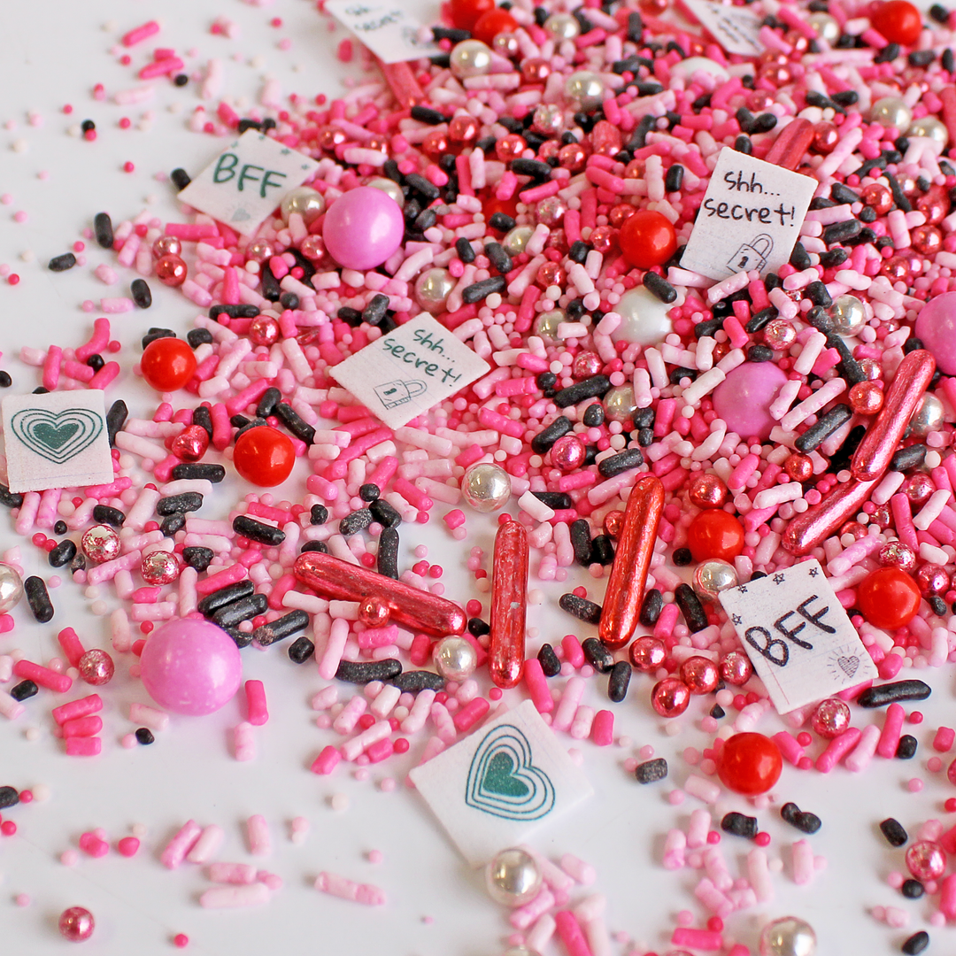 "So Fetch Sprinkle Mix with pink and black sprinkles and wafer paper notes for a 'Mean Girls'-inspired cake decoration"