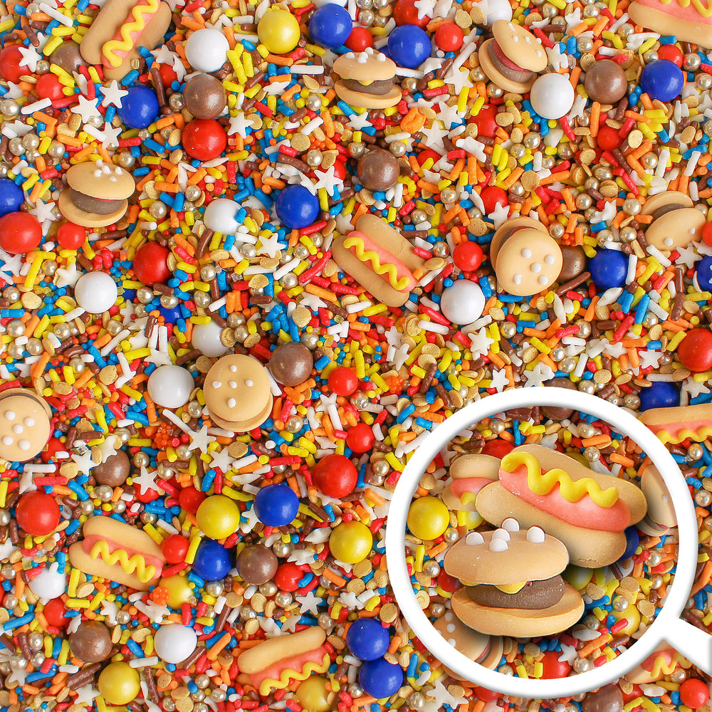 A photo of the Summer BBQ Sprinkle Mix featuring red, blue, and yellow sprinkles as well as royal icing hamburgers and hot dogs.