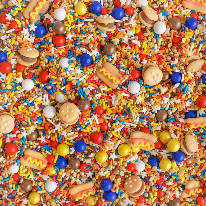 A photo of the Summer BBQ Sprinkle Mix featuring red, blue, and yellow sprinkles as well as royal icing hamburgers and hot dogs.
