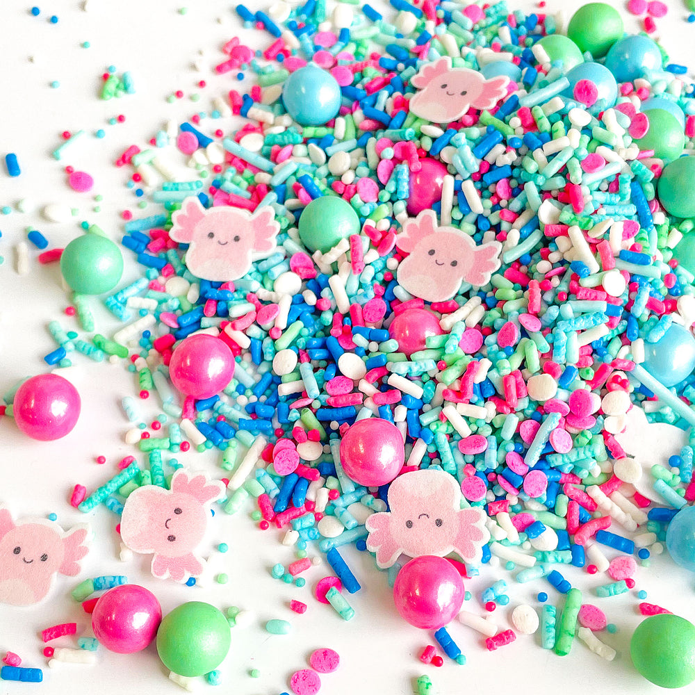 A close-up of Baby Axolotl Sprinkle Mix, featuring pink and blue sprinkles with adorable wafer paper baby axolotls, perfect for birthday cakes and treats.