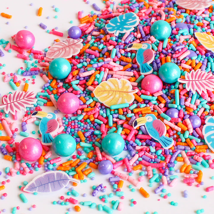 Birds In Paradise Sprinkle Mix - A vibrant blend of aqua, pink, purple, and orange sprinkle shapes with tropical birds and palm fronds.