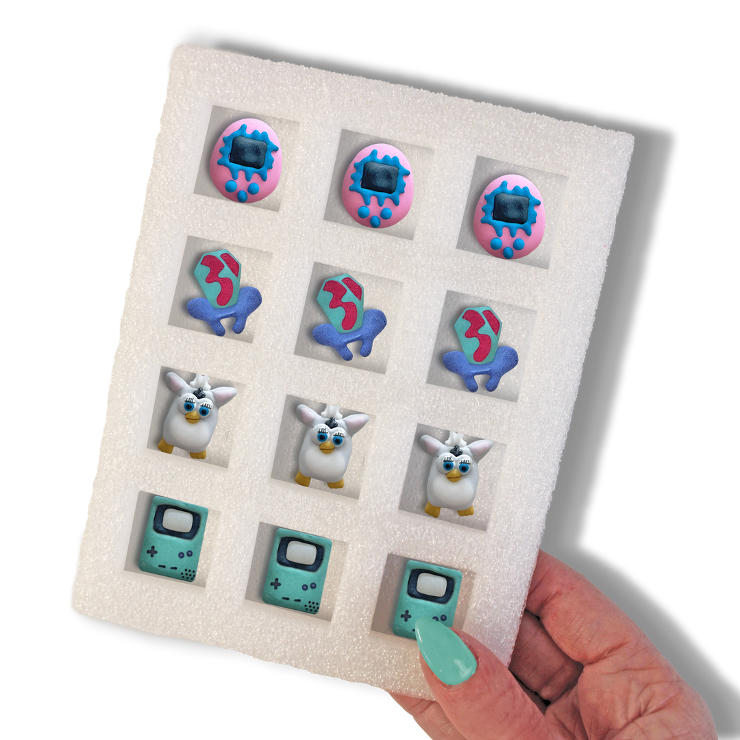 90's Collection set of hand-piped royal icing featuring a ring pop, a tamagachi, a furby and a gameboy