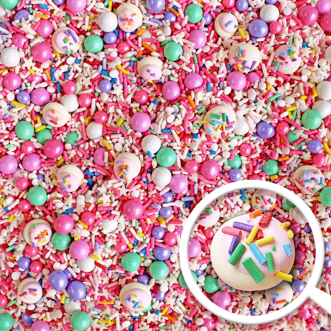 A close-up of a sprinkle mix featuring pink sprinkles and a rainbow of birthday sprinkles, along with hand-piped sprinkle cookies on top.