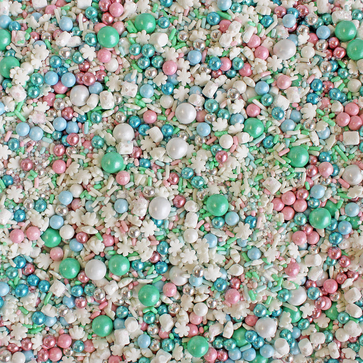 A whimsical winter sprinkle mix featuring soft pink, minty green, and baby blue sprinkles, snowflake confetti, metallic crispy dragees, and tiny marshmallows – a pastel-infused delight for festive desserts.
