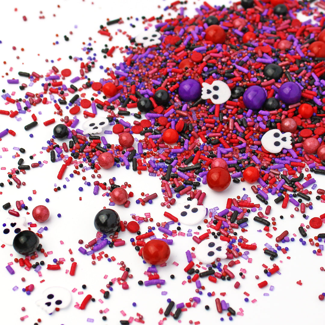 A close-up of Witch Doctor sprinkle mix featuring deep burgundy, reds, purples, blacks, and eerie wafer paper skulls.